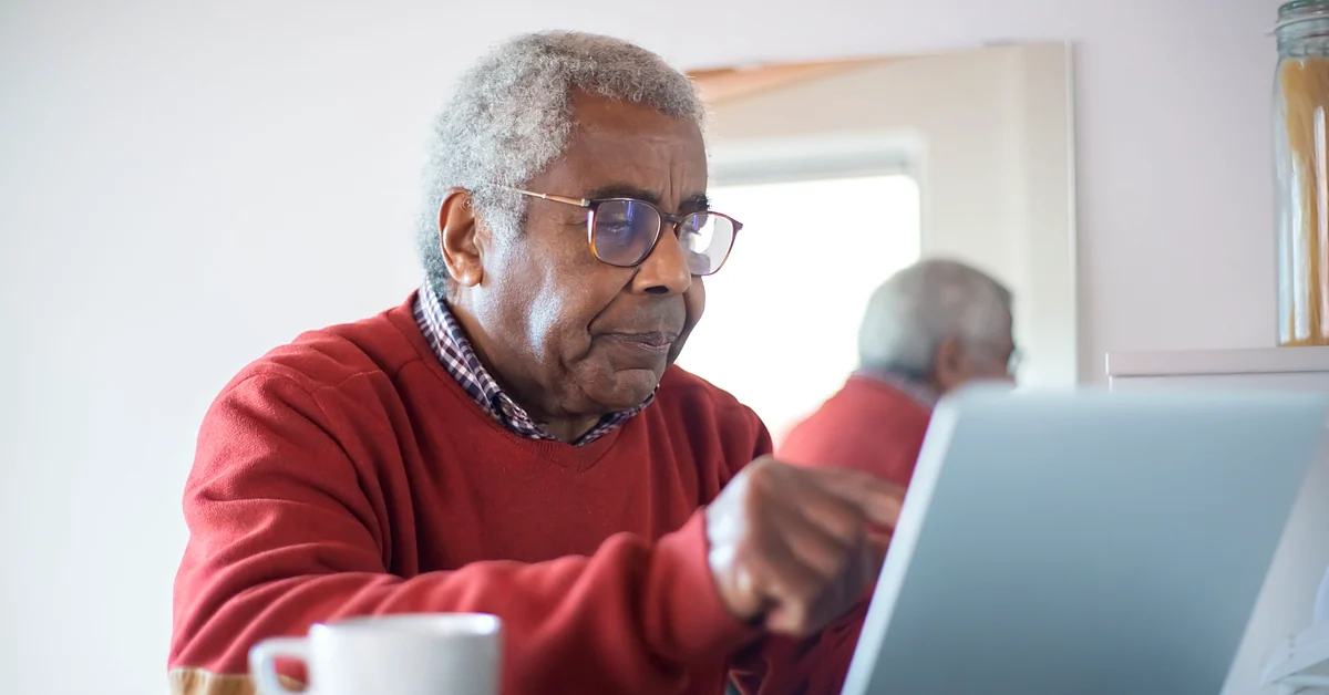 Older man wearing eyeglasses reviewing content on a laptop at home.