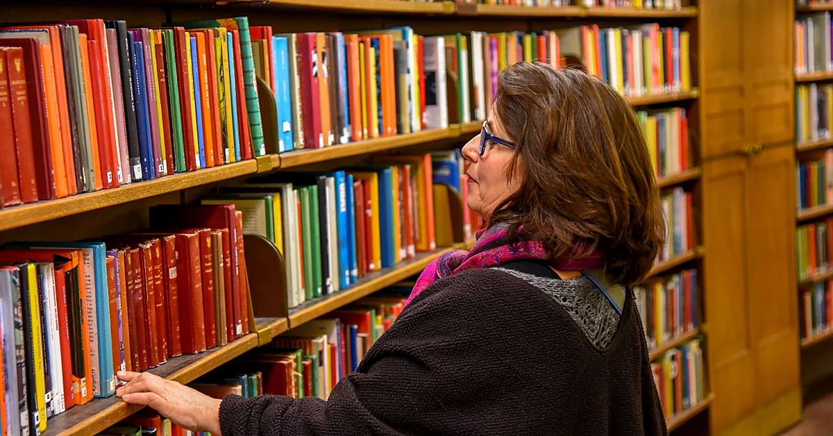 Woman browsing organized library bookshelves, illustrating how affiliate blog categories help readers discover relevant content.