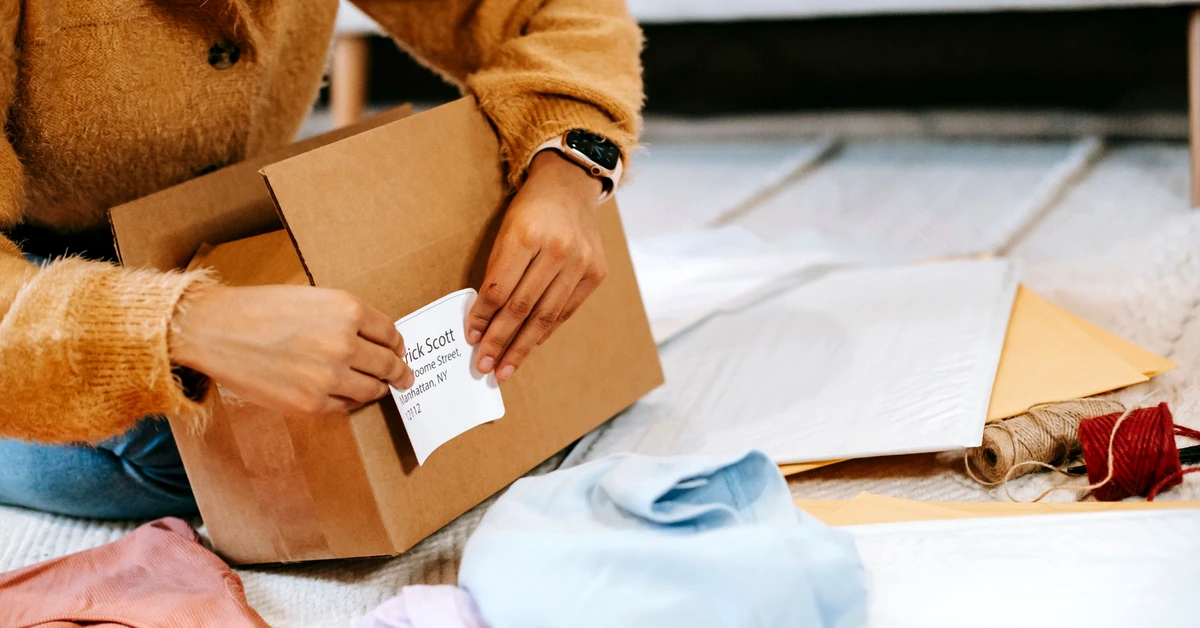Woman attaching a shipping label to a cardboard parcel, illustrating the product-return process that can affect affiliate commissions.