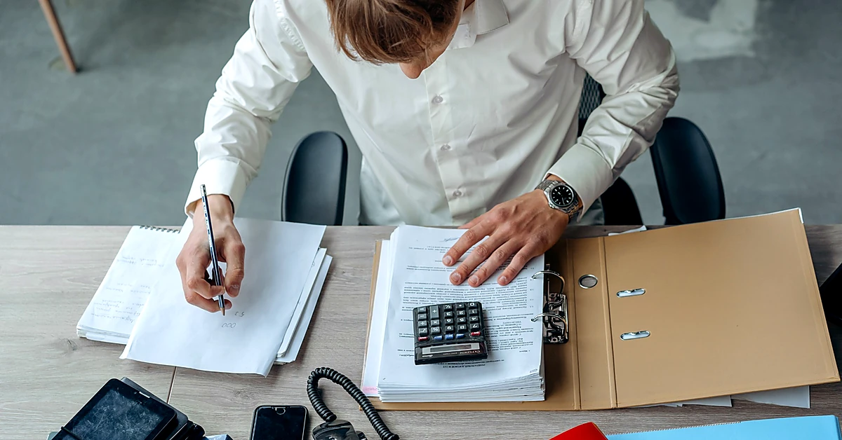 Professional reviewing financial documents and writing notes beside a calculator, representing affiliate commission verification.