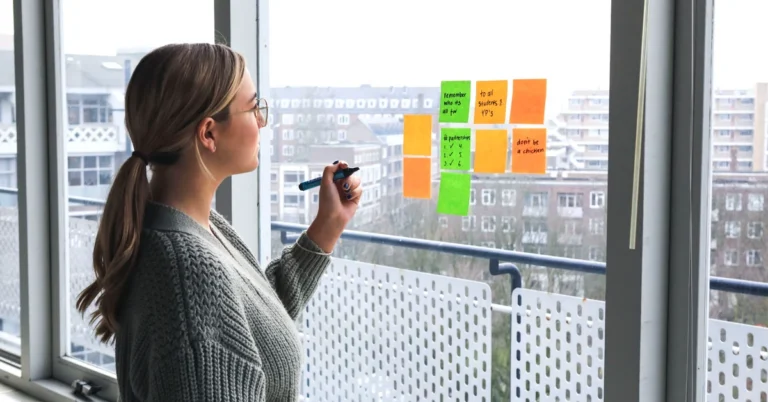 Woman reviewing colorful sticky notes on a window while organizing ideas for an affiliate content brief.