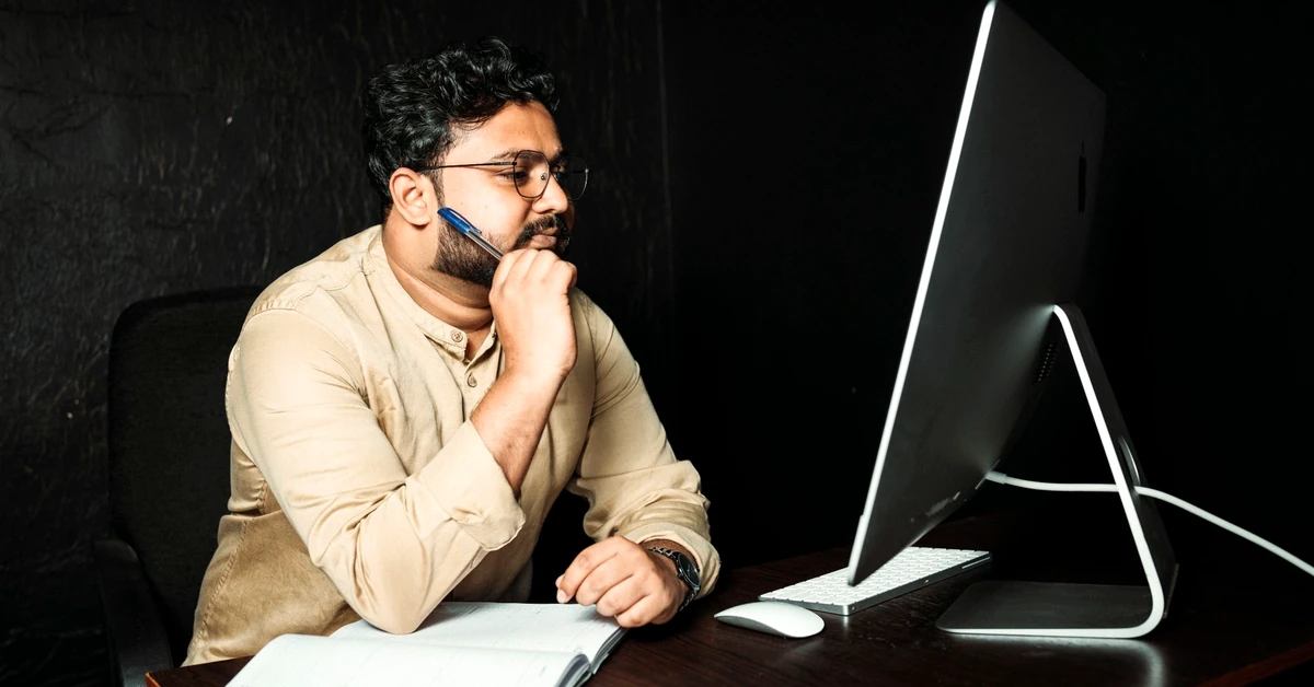 Man wearing glasses carefully reviewing information on a computer screen during a final content quality check.