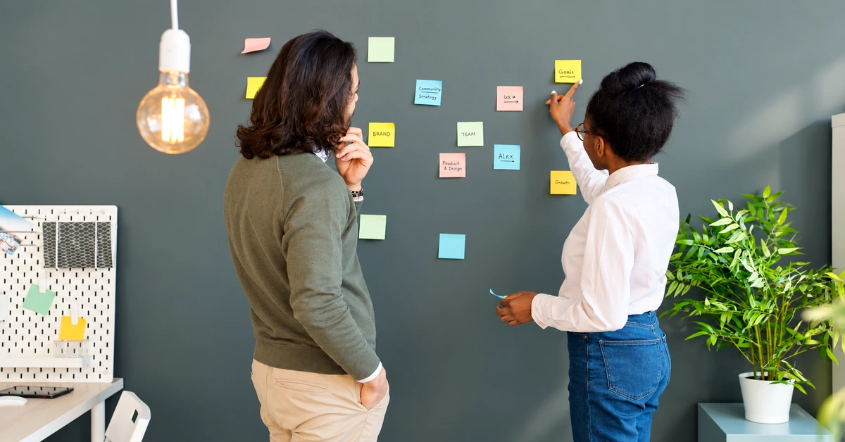 Two coworkers organizing colorful sticky notes to plan related topics for an affiliate content cluster