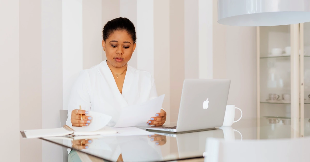 Woman reviewing documents beside a laptop while checking information before publishing affiliate content
