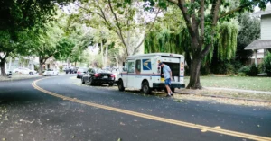 Mail carrier working from a postal van on a neighborhood route, illustrating the value of sending affiliate emails on a consistent schedule.