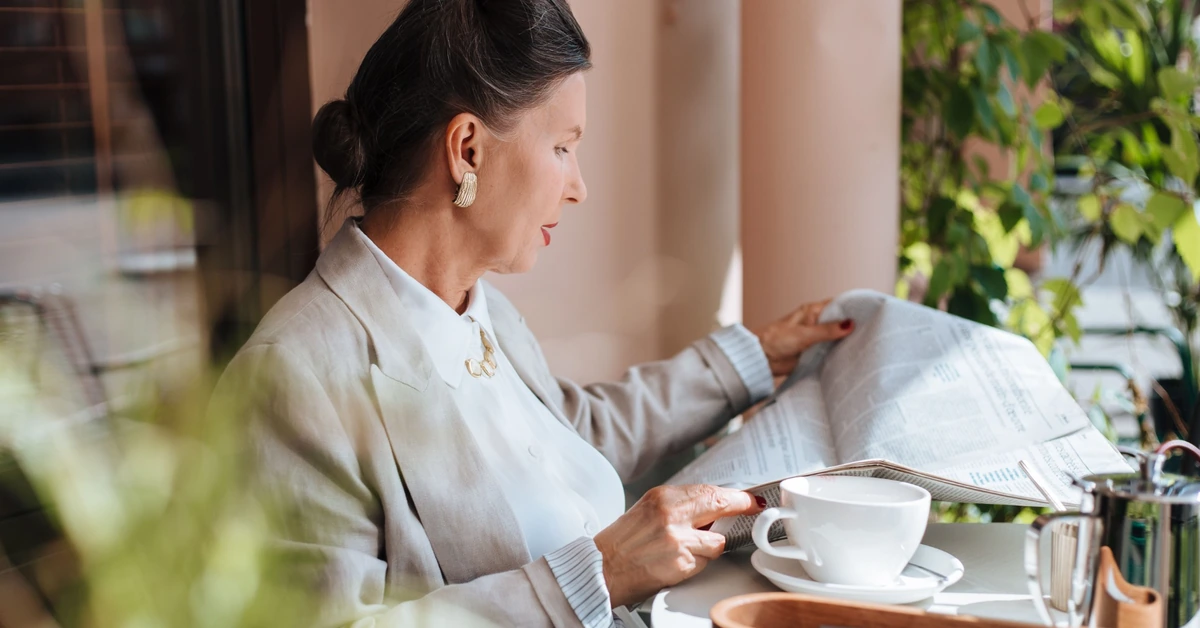 Woman reading a newspaper at a café, illustrating how an email broadcast can bring timely new content to an existing audience.