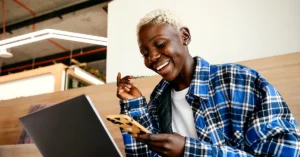 Smiling woman checking her smartphone while working beside a laptop in a modern workspace.
