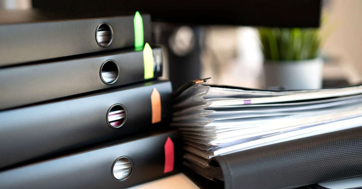 Black ring binders with colorful index tabs beside organized documents, representing structured email list management and unsubscribe records.