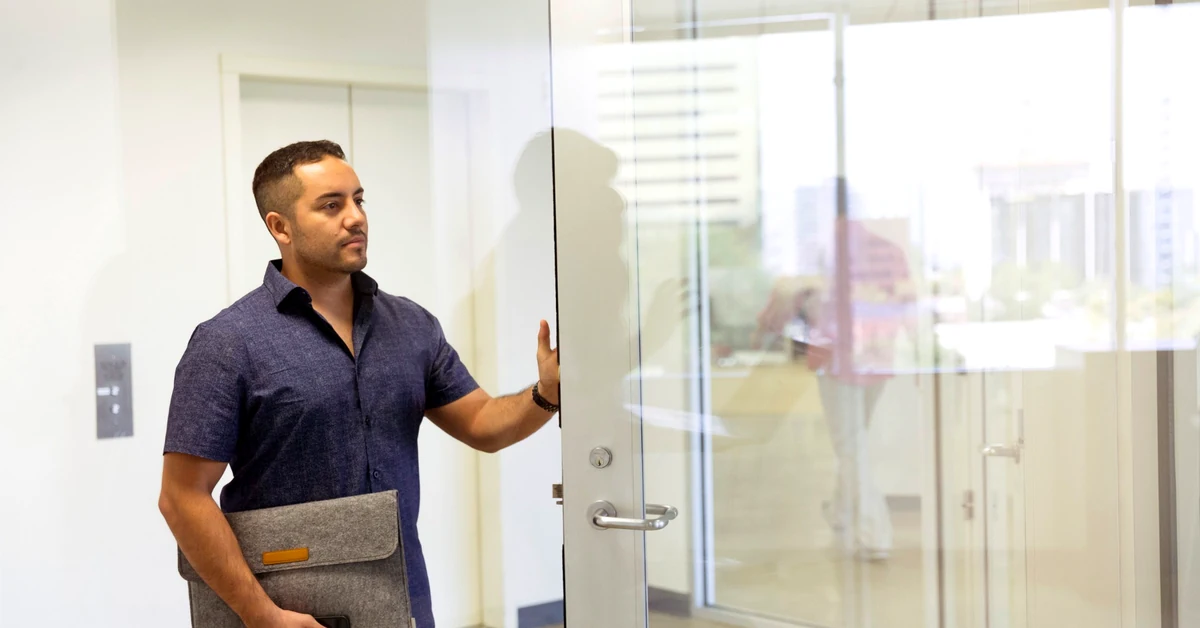 Professional man standing at an open glass office door, representing the freedom to leave an email subscription.