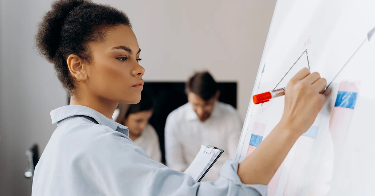 Businesswoman reviewing performance data on a whiteboard during a team meeting