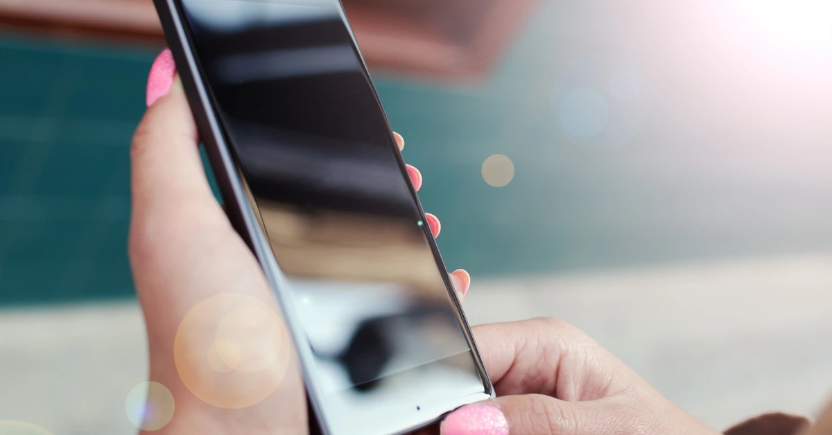 Hands holding a smartphone outdoors in bright light, illustrating the importance of testing an affiliate opt-in form on a mobile device.