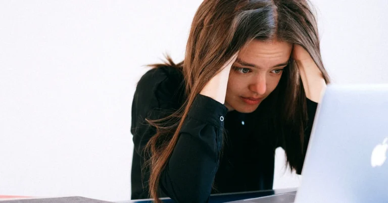 Concerned woman holding her head while reviewing information on a laptop after an unexpected setback.