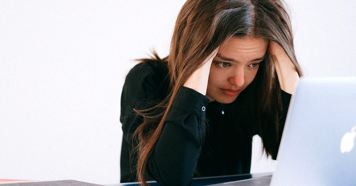 Concerned woman holding her head while reviewing information on a laptop after an unexpected setback.