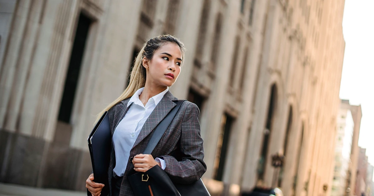 Professional businesswoman carrying a portfolio and shoulder bag on a city street, representing moving forward after an affiliate program rejection.