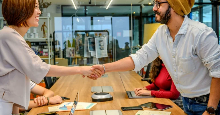 Affiliate marketing partners shaking hands during a team meeting while evaluating a joint venture opportunity