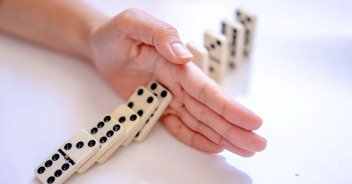 Hand stopping falling dominoes, representing improving one weak point in an email funnel at a time.