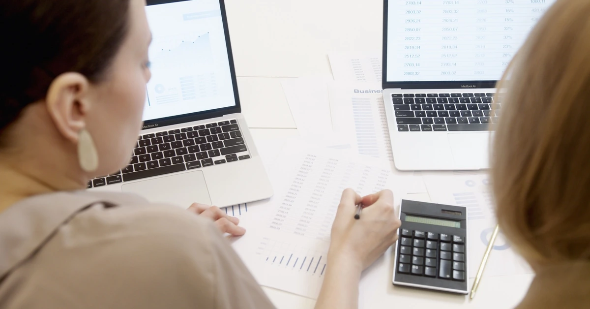 Two people reviewing charts, spreadsheets, and laptop screens, illustrating how ClickBank Marketplace metrics should be analyzed in context.