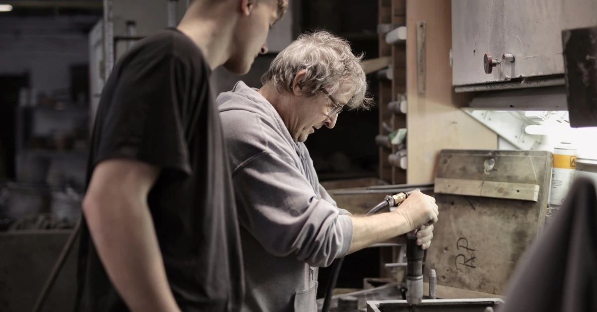 Experienced craftsman teaching an apprentice at a workshop bench, illustrating how affiliate marketing training becomes useful when it is put into practice.