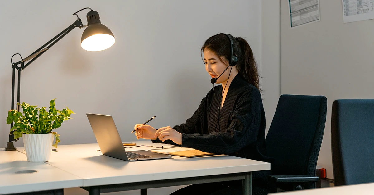 Female customer support representative wearing a headset while reviewing account information at a laptop.