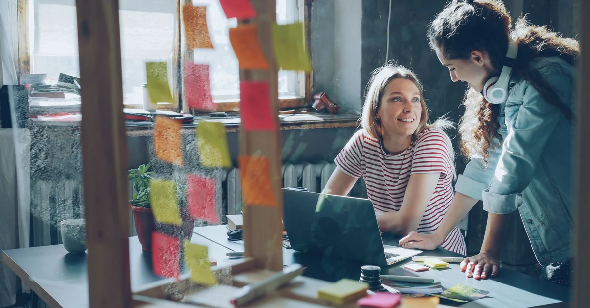 Two professionals collaborating with laptops and sticky notes while planning a reusable landing page workflow.