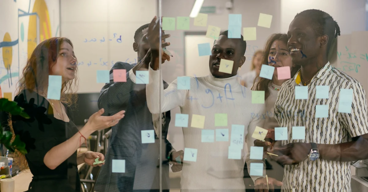 Diverse professionals planning a multistep marketing workflow using sticky notes on a glass wall.