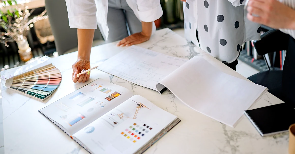 Colleagues reviewing printed layouts and color samples spread across a bright office worktable.
