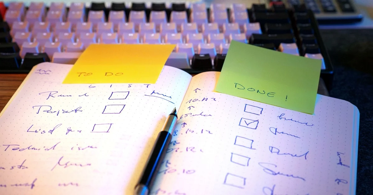 Open handwritten checklist with yellow TO DO and green DONE sticky notes beside a computer keyboard and pen.