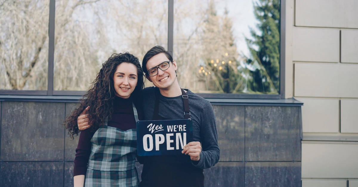 Two small business owners standing together with an open sign, illustrating how a personal identity and a business brand can work together.