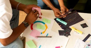 Two colleagues reviewing colorful charts, printed reports, and sticky notes while planning together at a table.