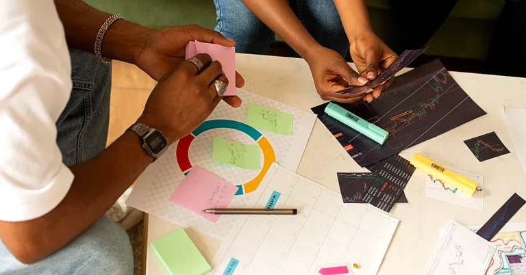 Two colleagues reviewing colorful charts, printed reports, and sticky notes while planning together at a table.